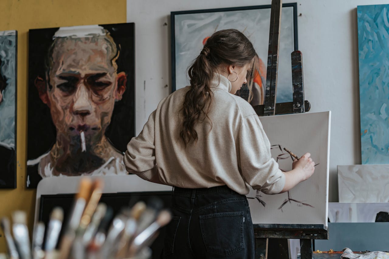 Female artist working on a canvas in a studio with paintings in the background.